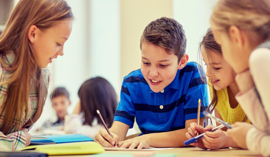 Kinder sitzen am Tisch und machen eine Gruppenarbeit